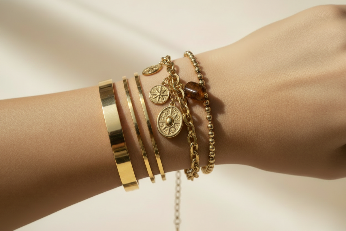 Styled gold bracelet stack on a wrist featuring a Roman coin charm bracelet, two slim gold bangles, and a beaded bracelet with amber stone charms
