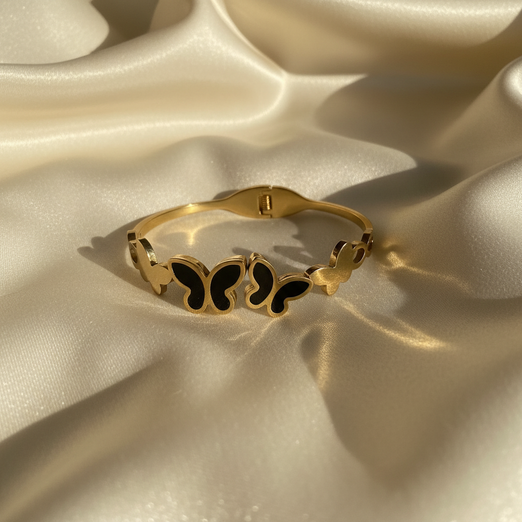 18K gold plated black butterfly cuff bangle with black enamel butterfly motifs laid flat on cream satin fabric — Bangle Bangle