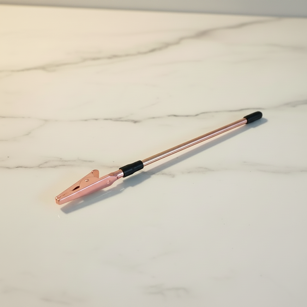 Rose gold bracelet helper tool with alligator clip and rubber tip on a white marble surface — Bangle Bangle