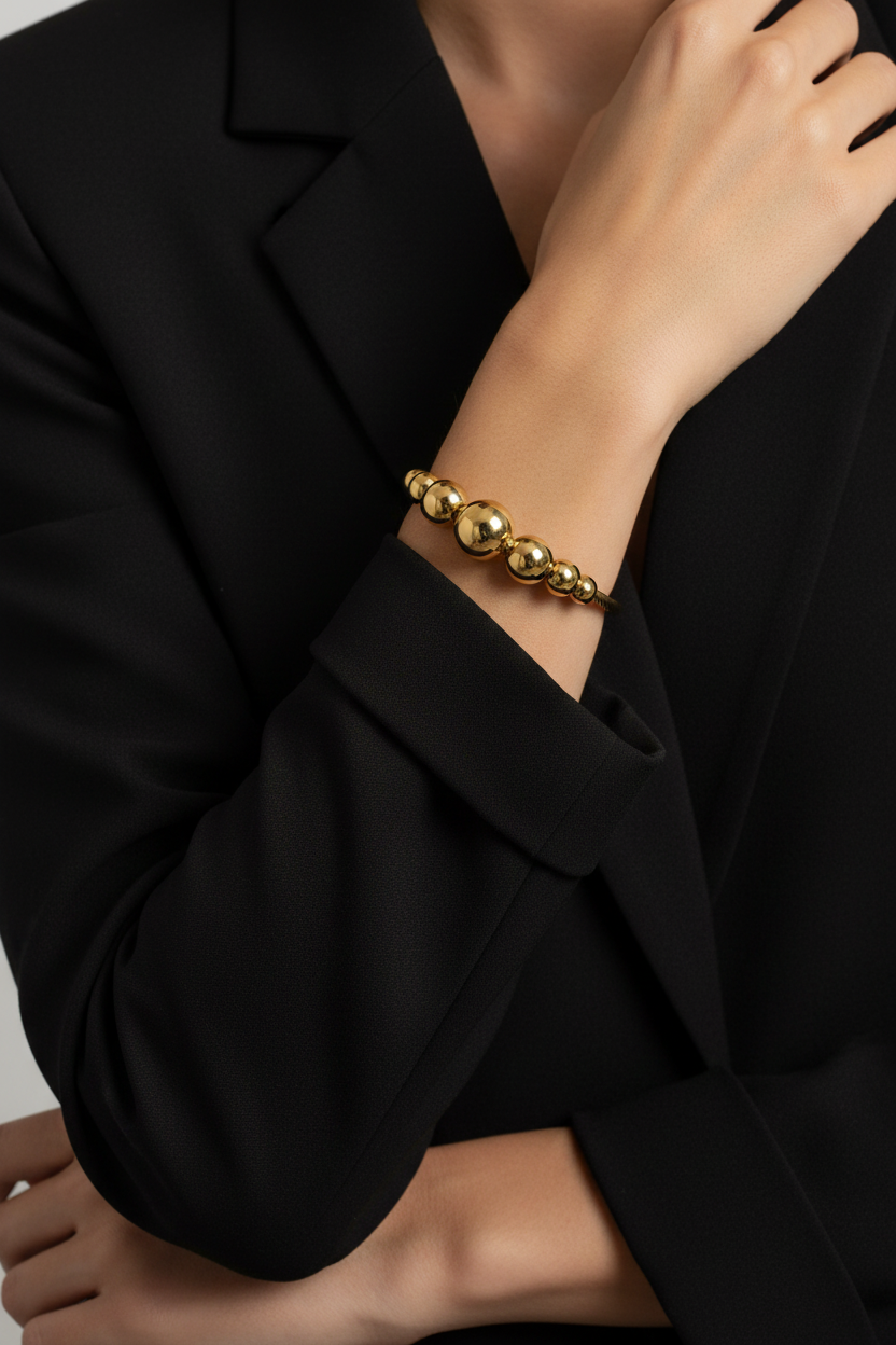 18K gold plated graduated ball cable cuff bangle worn on a woman's wrist with black blazer sleeves pushed up — Bangle Bangle