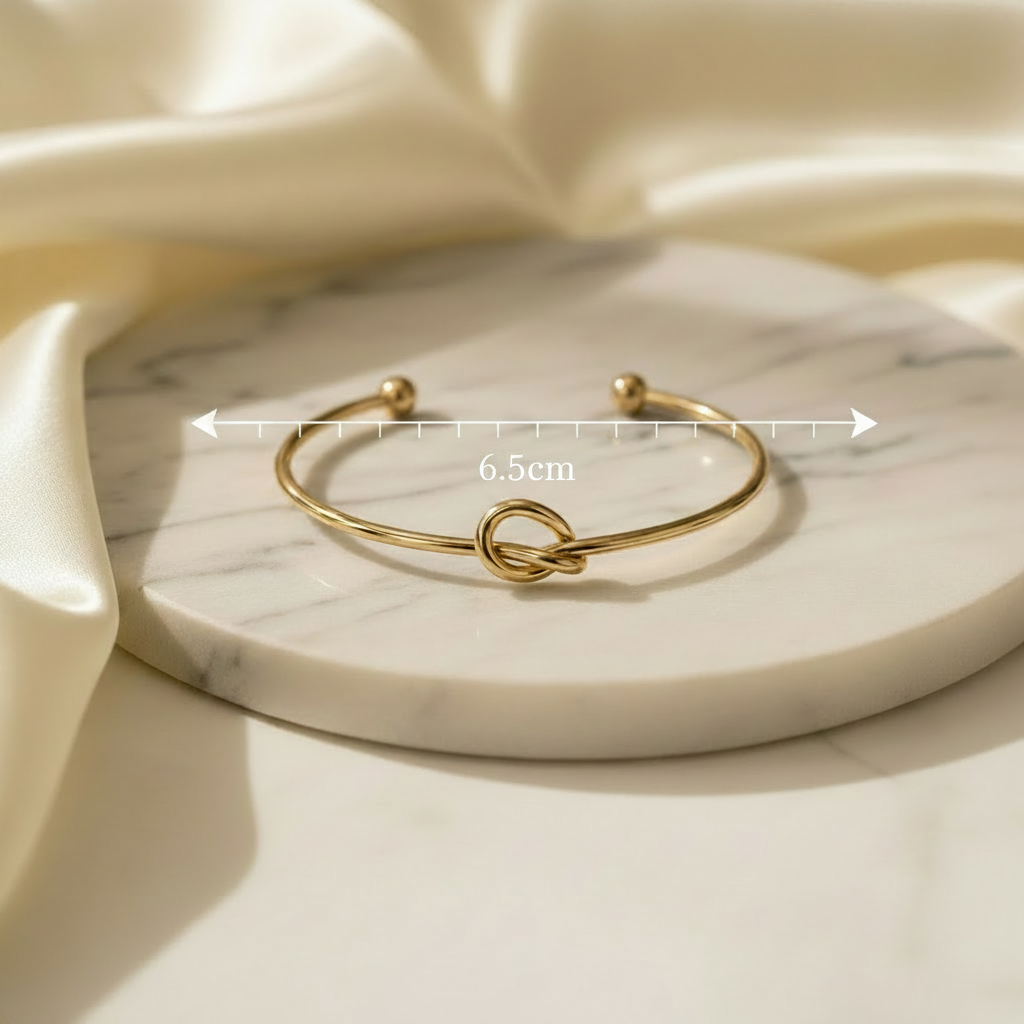 18K gold-plated knot cuff bracelet on white marble with double-headed arrow showing 6.5cm internal width measurement