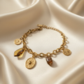 18K gold plated Roman charm bracelet with mixed gold charms laid flat on cream satin fabric — Bangle Bangle