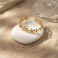 18K gold-plated starfish open cuff bangle resting on a smooth white stone, warm sandy background, luxury jewelry photography