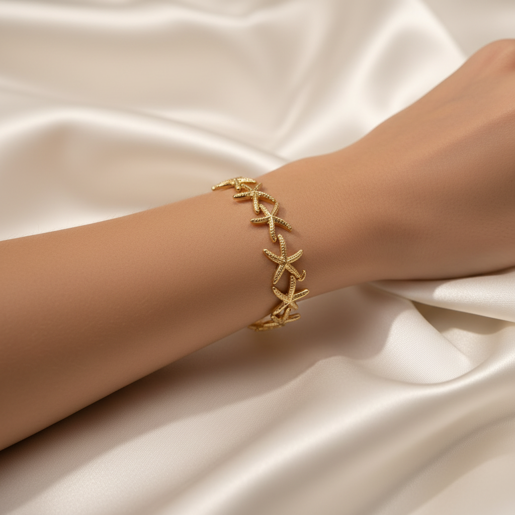 18K gold-plated starfish cuff bangle worn on a woman's wrist with soft white fabric background, close-up editorial jewelry shot