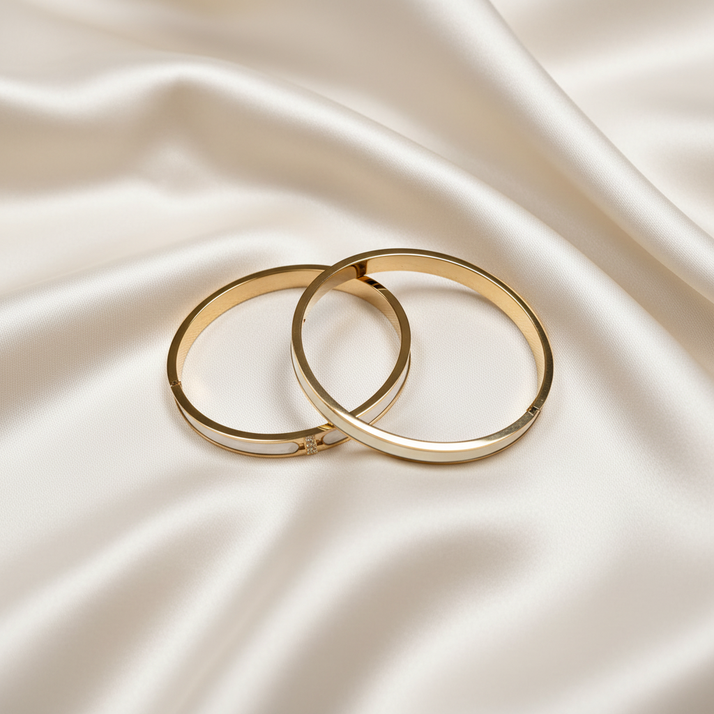 18K gold-plated white inlay bangle set of 2 stacked together on soft cream silk fabric, overhead flat lay, luxury jewelry photography